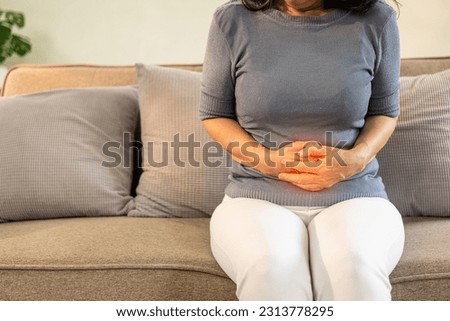 Asian old woman sitting on sofa with stomach ache irritable bowel syndrome Abdominal pain in the elderly, flatulence, inflammatory bowel disease, health care Royalty-Free Stock Photo #2313778295