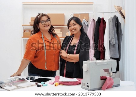 Portrait of smiling two asian  female fashion designer at desk in studio