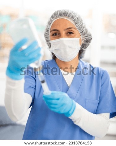 Female nurse in a protective mask, working in the clinic in the treatment room, fills a syringe with medicine with ..saline solution for injection