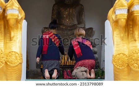 The backs of men and women in traditional Thai costumes are sitting and lighting incense sticks. Worship Buddha images together.