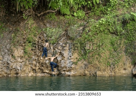 two Asian boys are trying to climb a cliff by the river