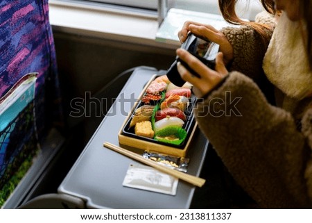 Asian woman using digital camera taking picture of traditional Japanese lunch box bento during travel on train. Attractive girl travel Japan on railroad transportation on winter holiday vacation.