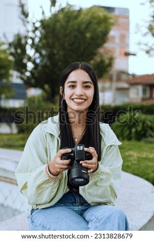 Portrait of a young woman in her 20's with a professional camera on a sunny afternoon in a park in South America.