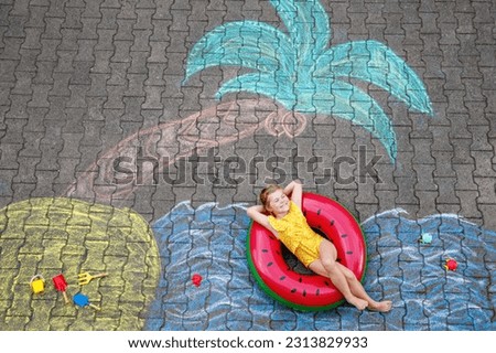 Happy little preschool girl in swimsuit on inflatable ring with sea, sand, palm painted with colorful chalks on asphalt. Cute child with having fun with chalk picture. Summer, vacations, summertime