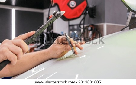 A specialist repairs a dent on the car body without painting. PDR. Process of paintless dent repair on car body. The mechanic at the auto shop with tools to repair dents in car body. Body repair. Royalty-Free Stock Photo #2313831805