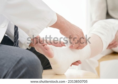 Asian doctor bandaging a woman's leg, no face Royalty-Free Stock Photo #2313850705
