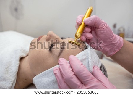 Young woman lying on cosmetologist's table and applying procedure with vibration massager on face. Skincare lifting at spa Royalty-Free Stock Photo #2313863063