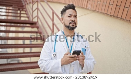 Young latin man doctor using smartphone at hospital