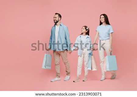 Full body side view happy young parents mom dad with child kid daughter teen girl in blue clothes holding package bags with purchases after shopping go isolated on plain pastel light pink background.
