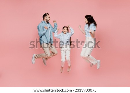 Full body young parents mom dad with child kid daughter teen girl in blue clothes jump high do winner gesture clench fist look to each other isolated on plain light pink background. Family day concept