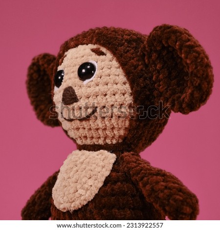 Children toy soft knitted brown Cheburashka on pink background. DIY concept. Handmade work. Hobbies needlework sewing and knitting with woolen threads. Character in Soviet Russian cartoon. Side view.