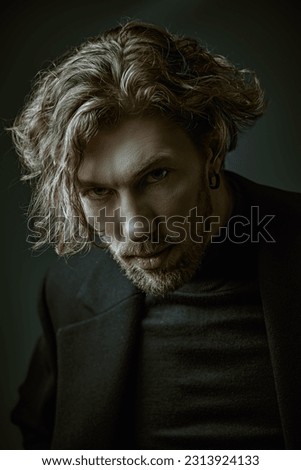 Psychological picture. Art portrait in a dark key of a handsome forty-year-old man with curly hair, dressed in a black pullover, who looks directly and thoughtfully into the camera. People, emotions. 
