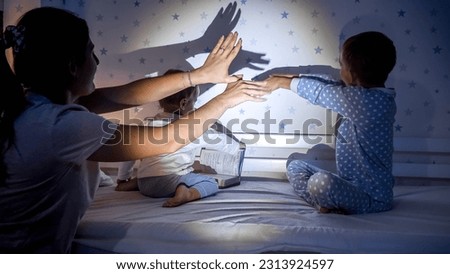 Two boys in pajamas and mother playing with shadows from flashlight in bedroom at night. Family having time together, parenting, happy childhood and entertainment