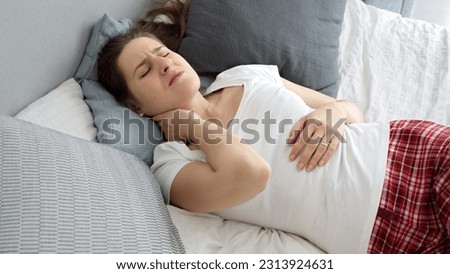 Portrait of young woman in pajamas suffering from pain in neck after sleeping on uncomfortable pillow. Concept of healthcare problems, pain relief and injuries Royalty-Free Stock Photo #2313924631