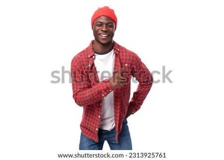 handsome young american man in red cap and plaid shirt pointing with finger on white background with copy space