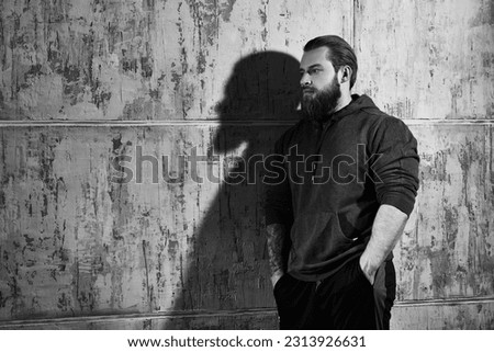 A large, strong man stands leaning against a concrete wall, lost in thought. Black-and-white portrait. Place for text. Psychological picture.