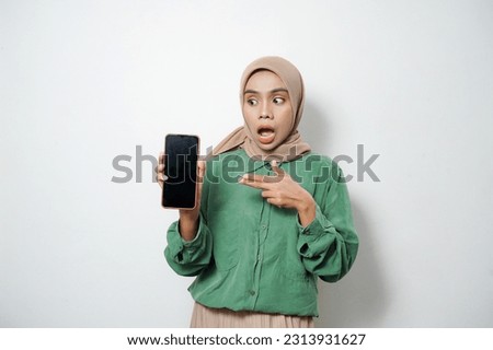 Shocked young Asian Muslim woman dressed in casual showing blank screen mobile phone, recommending mobile app