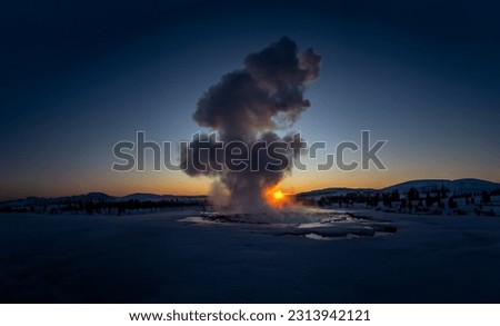 Iceland's great geyser Strokkur in full eruption with mist and smoke backlit and the orange evening or near-dusk sun touching the horizon behind