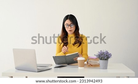 An intelligent and nerdy young Asian female college student in glasses focused on reading a book at her desk. isolated on a white background