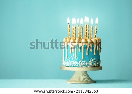 Elegant turquoise birthday cake with gold drip icing and gold birthday candles against a turquoise background Royalty-Free Stock Photo #2313942563