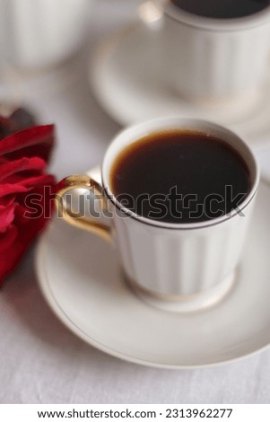 A server with a coffee service and a red rose on a white rag background. The cups are filled with black coffee.