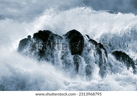 Detailed photo of a big stormy wave crashing over a boulder