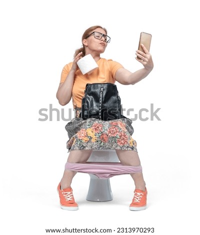 Funny young woman with glasses takes a selfie sitting on the toilet and holding a roll of toilet paper in her hand, isolated on white background
