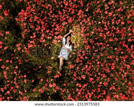 Beautiful girl posing in a poppy field. A woman in a white dress stands among the flowers. The young girl smiles. The concept of happiness. Rest in a summer meadow of poppy flowers