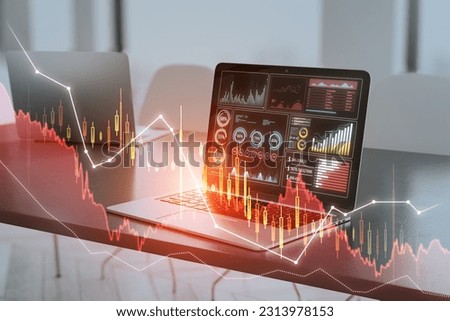 Close up of laptop at desk with downward candlestick forex chart on blurry backdrop. Trade, finance and technology concept. Double exposure
