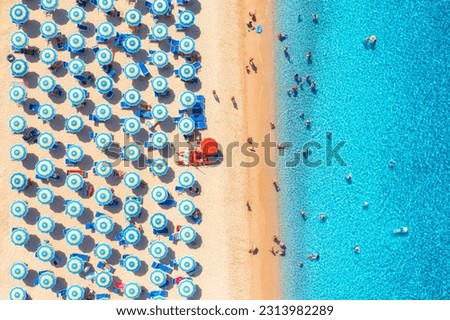 Aerial view of colorful umbrellas on sandy beach, swimming people in blue sea at summer sunny day. Resort in Sardinia, Italy. Tropical seascape with turquoise water. Travel and vacation. Top view