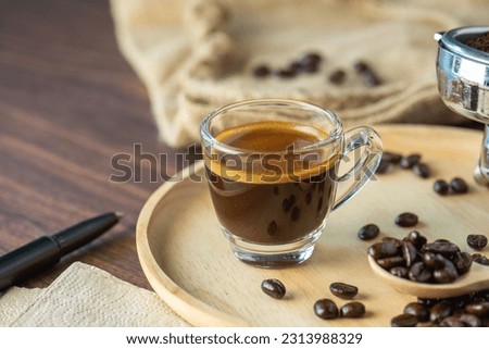 cup of hot Intense coffee dark shot in glass on wooden table with beans with crema. coffee beans and cup full of Intense dark shot coffee in glass cup Royalty-Free Stock Photo #2313988329