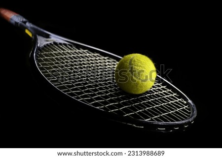 A tennis racket hangs in the air across the frame, and a green tennis ball is on it, photographed in a spot of light against a black background Royalty-Free Stock Photo #2313988689