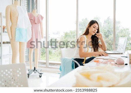 Beautiful Asian female fashion designers or dressmakers make the design of the new collection with samples of fabrics and sketches on paper. Fashion designer working in studio. Small business concept.