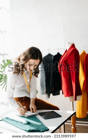 Caucasian young woman on desk in office of fashion designer and holds tablet, laptop and smartphone.