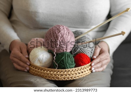 Senior woman's hands holds a wicker basket with clews and skeins of yarn for knitting, knitting needles. Craft and DIY.