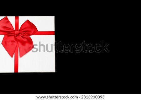 White gift box with a red ribbon and a bow on a black background. Gift for birthday or traditional holiday. Gift box close-up. Free space for text or image