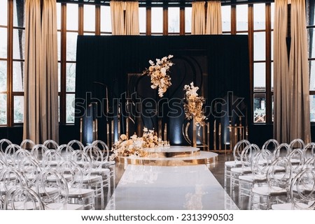 Wedding. Decor. In the hall for the wedding ceremony there are transparent chairs for guests and a podium decorated with compositions of colorful flowers and golden branches Royalty-Free Stock Photo #2313990503