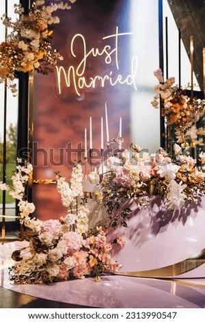 Wedding. Decor. In the festive hall bride and groom's table is decorated with comositions of flowers and golden branches, on the table candles and glasses. In the background the sign "Just married"
