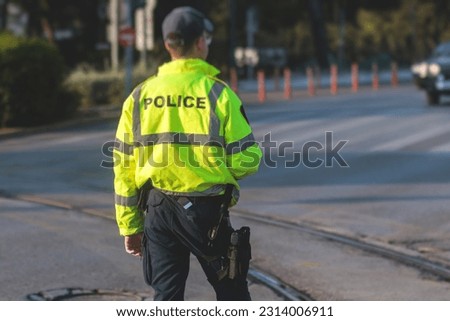 Inspector of traffic police highway patrol regulates the movement of transport in the center of european city, in green yellow vest jacket with a sign "Police", police officer control road traffic