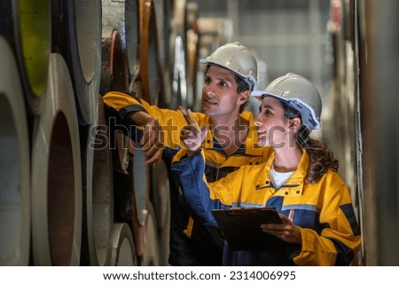 two young engineer assistant in helmet inspection check heavy machine construction installation industrial metal roof roll sheet factory. colleague friend worker point finger check operation factory Royalty-Free Stock Photo #2314006995
