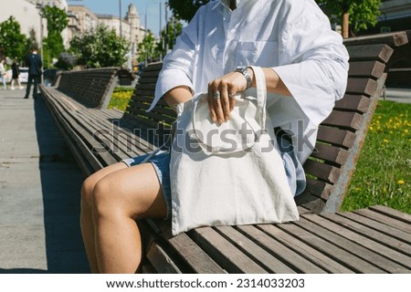 A girl open eco shop bag. Yound woman sitting on a bench in park with white tote canvas cotton shopper. Zero waste, reusable, healthy lifestyle. Place for text, logo, design