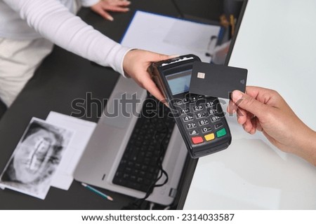 Top view customer hand holding a black mockup credit card above a POS terminal, making wireless or cashless payment using NFC technology. Close-up. Copy advertising space. People, business and finance Royalty-Free Stock Photo #2314033587