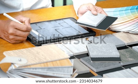 Architect hand choosing and picking stone and wood material samples while drawing on a digital tablet on the table in studio. Designer working for interior architecture and furniture design project.