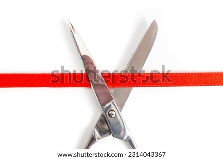 Stainless steel scissors cutting a red satin ribbon, close up isolated on white