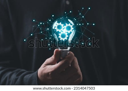 businessman Hand holding smart phone and light bulb with gear glowing with orange light and ray. Creative and new business knowledge thinking idea concept. Royalty-Free Stock Photo #2314047503