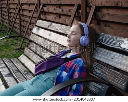 Blonde child purple headphones listen to meditation music podcast smartphone bench outside city street urban lifestyle.Concentrated young girl online audio book Mental health Stress relief digital app