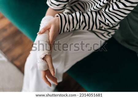 High-angle view cropped shot of unrecognizable young woman with broken right hand wrapped in white gypsum bandage, gently massaging injured wrist. Unhappy female with broken arm from accident at home. Royalty-Free Stock Photo #2314051681