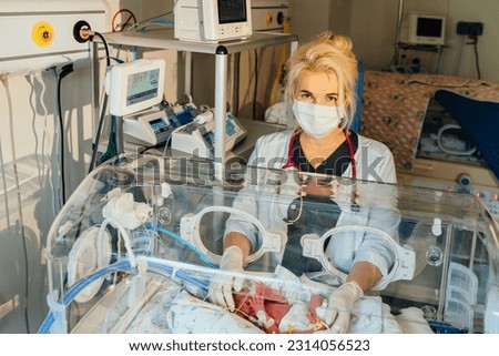 At the intensive care unit. Doctor standing near hospital bed with a baby preparing it for treatment. Newborn is placed in the incubator. Neonatal intensive care Royalty-Free Stock Photo #2314056523