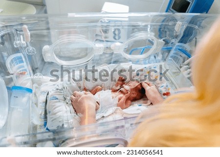Unrecognizable mother's hands holding new born baby born at 28 weeks gestation in intensive care unit in a medical incubator. Royalty-Free Stock Photo #2314056541