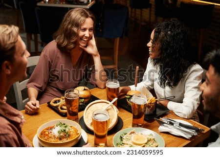 Happy young multiracial group of friends in casual clothing smiling during conversation over dinner Royalty-Free Stock Photo #2314059595